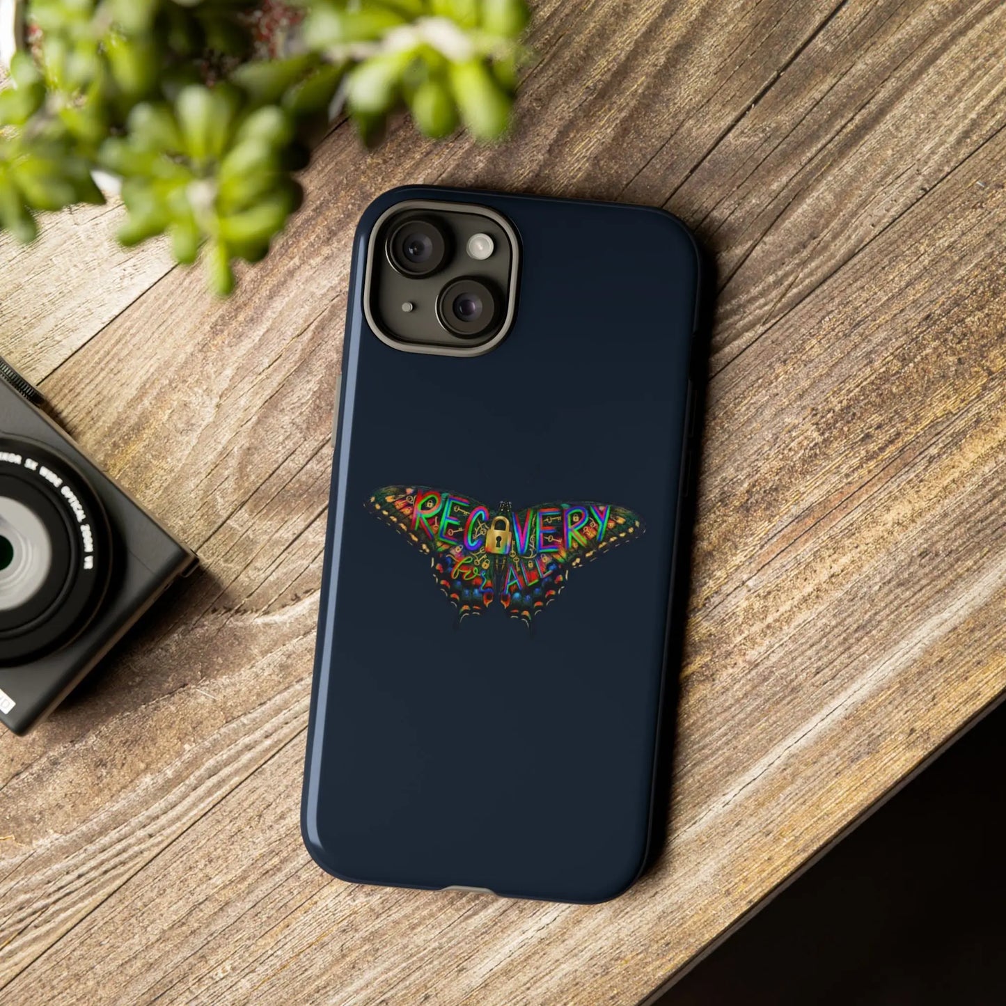 Phone case with colorful design on a wooden surface next to a camera and plant